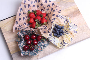 multiple beeswax wraps on a chopping board filled with fresh fruit